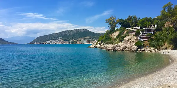 Plaka, a long beach with trees behind it and a few boats in shallow waters